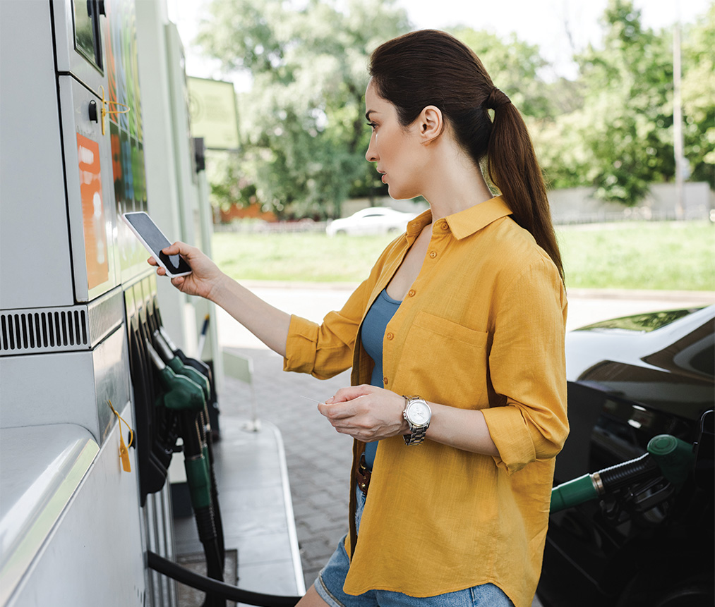 A woman checking her phone at a gas station fuel pump