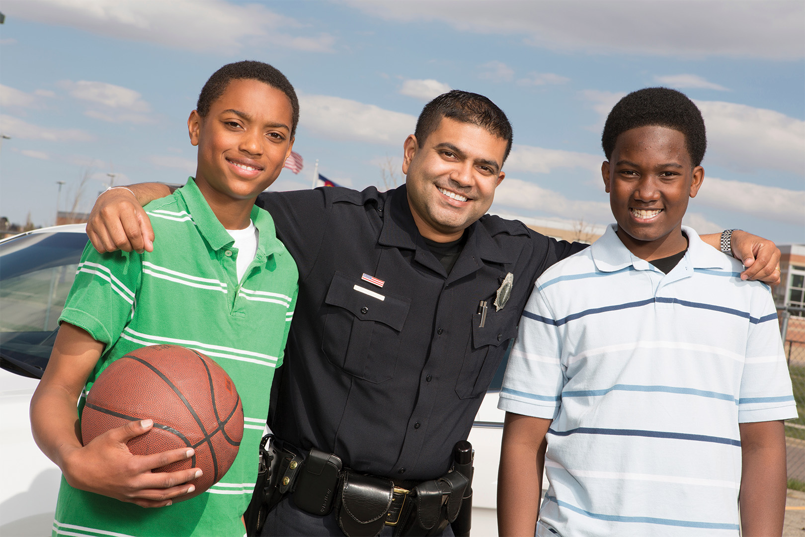 A police officer standing with two teenage boys, one holding a basketball